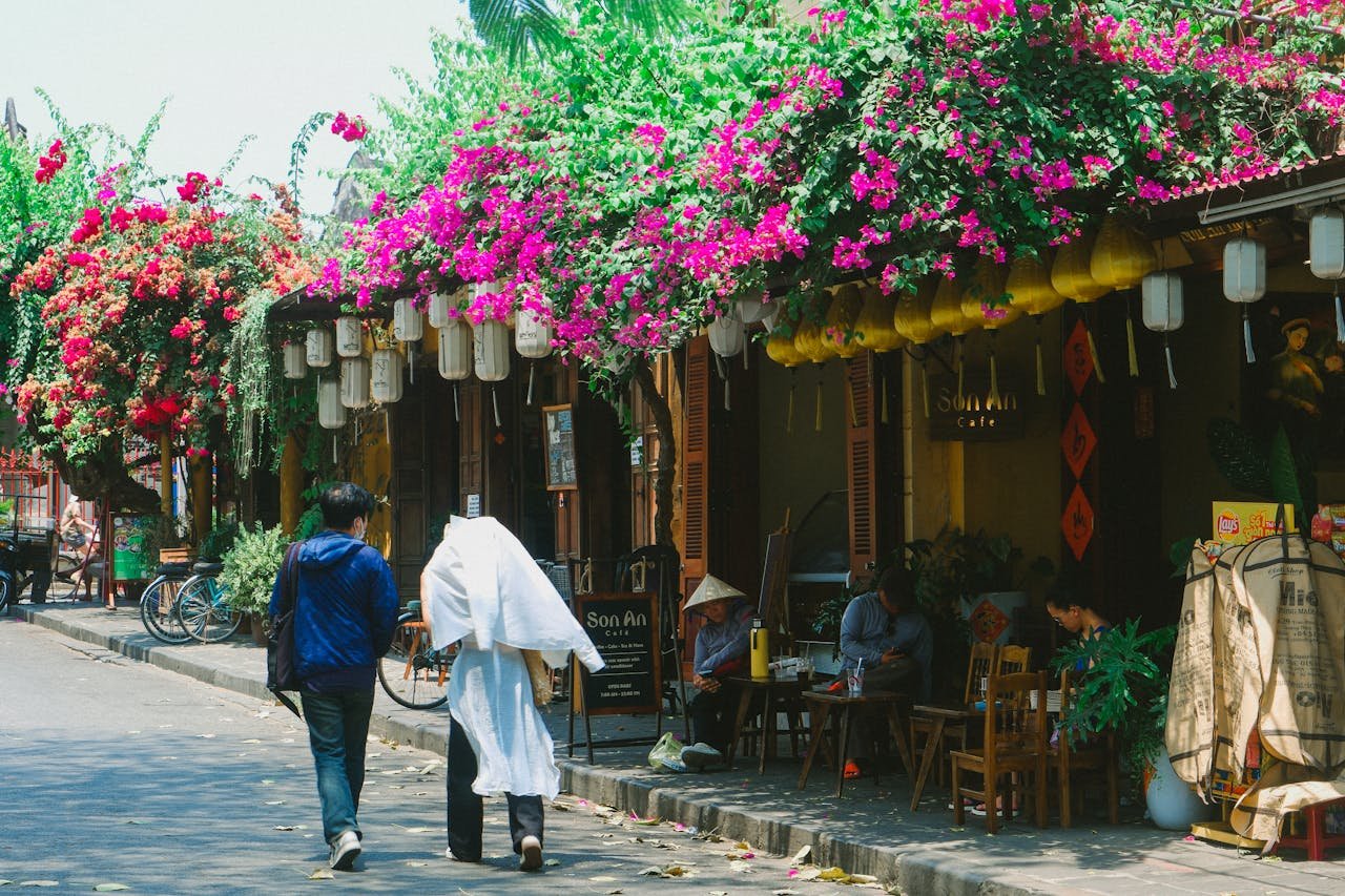 Vibrant street scene in Hoi An, Vietnam, featuring pedestrians and cafes under colorful bougainvillea.